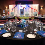 An event stage decorated with colourful lighting and soccer balls shaped in a wave behind the seats.